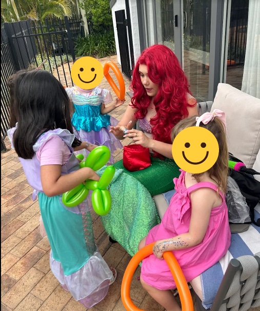 A Polished Parties entertainer making balloon animals with children at a garden party, children’s faces covered with smiley faces for privacy
