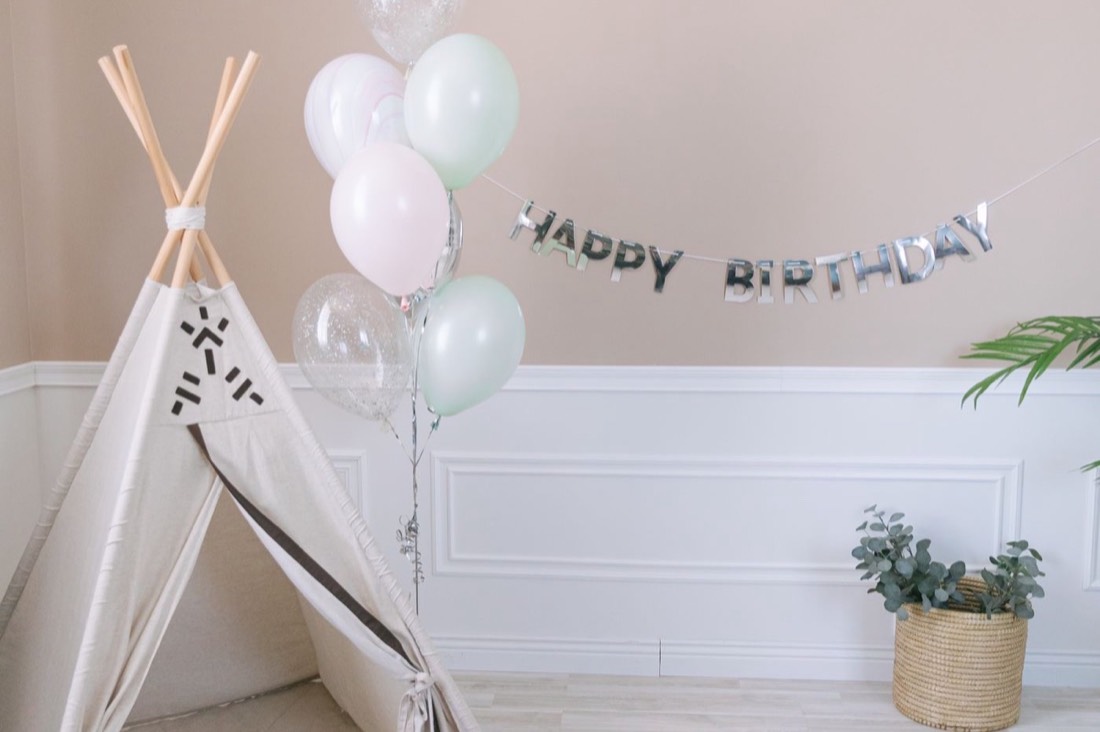 A pastel birthday setup with balloons, a teepee and gifts