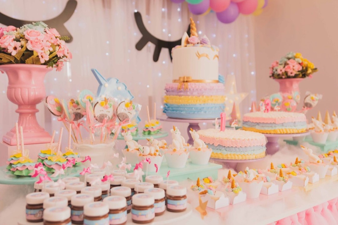 A pastel unicorn themed party table with cakes and treats
